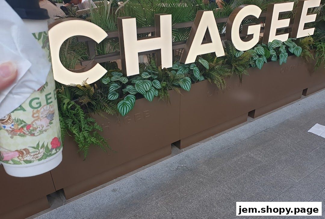 A hand holds a CHAGEE branded cup in front of the shop's illuminated sign.