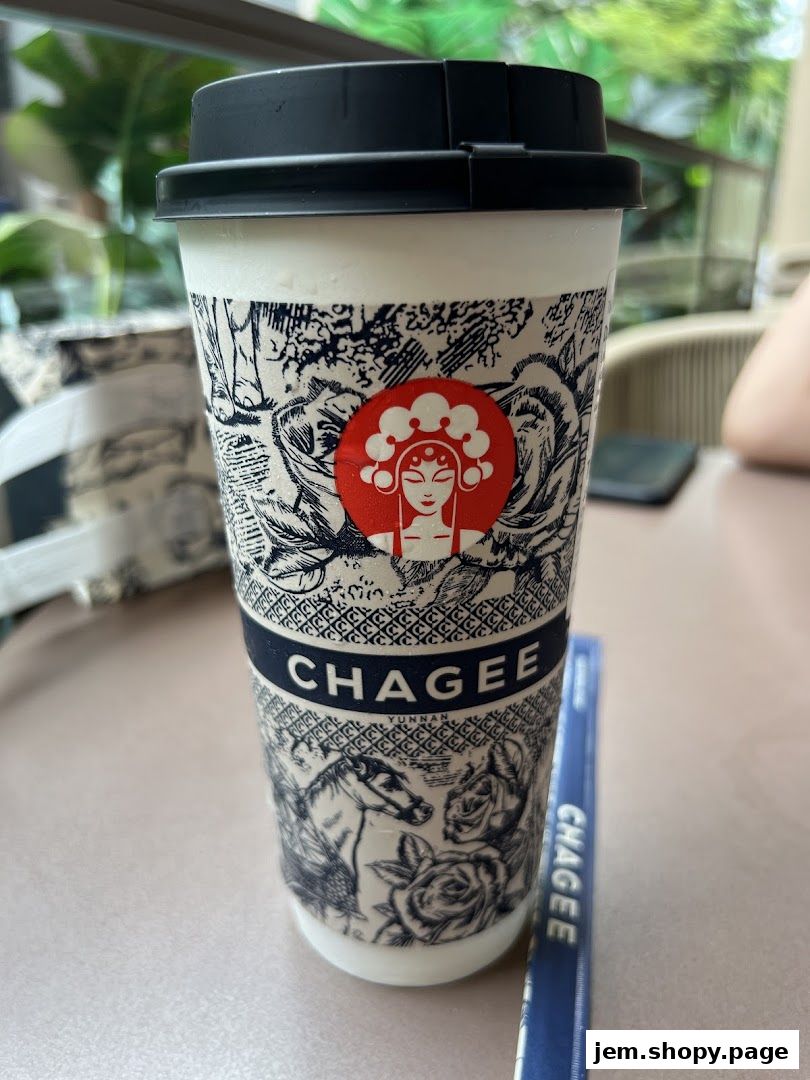 A CHAGEE branded cup with intricate designs and a black lid sits on a table.