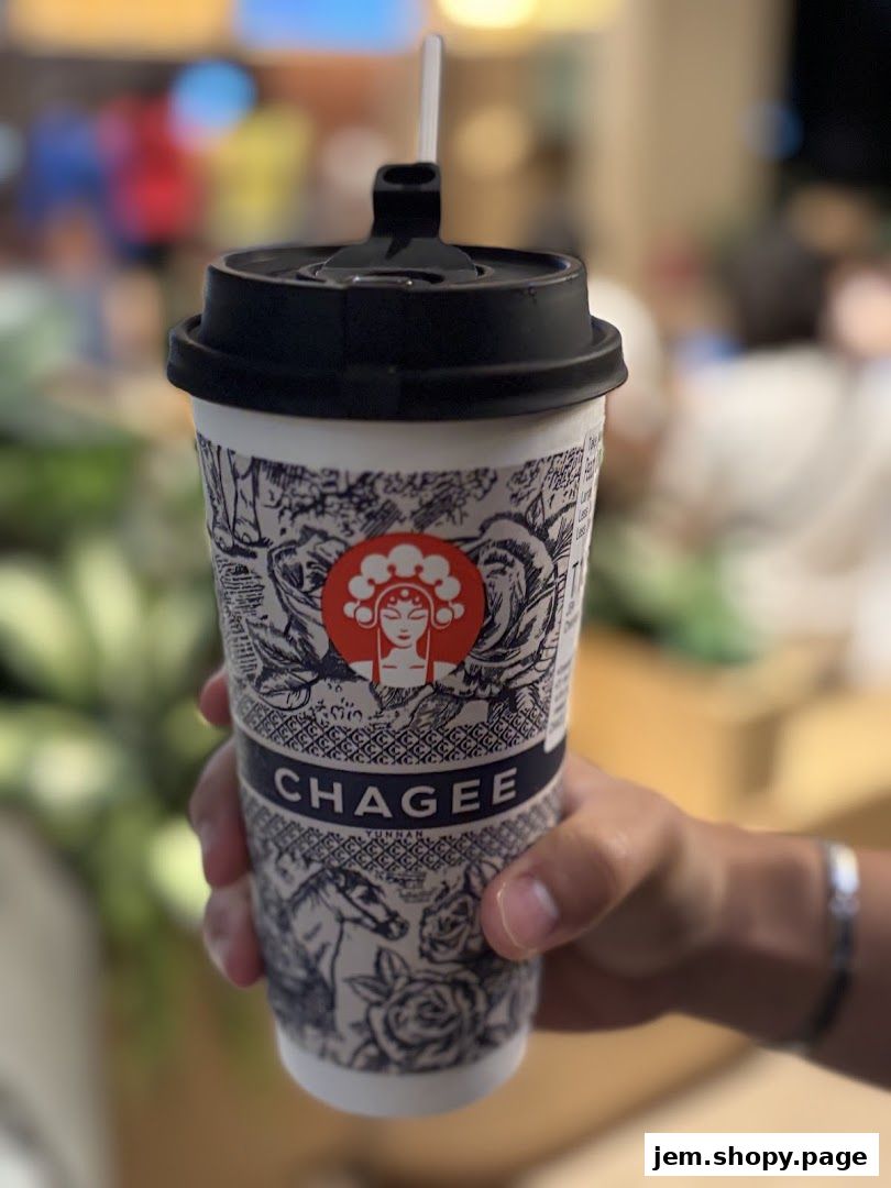 A hand holds a CHAGEE branded cup with a straw, featuring intricate designs.