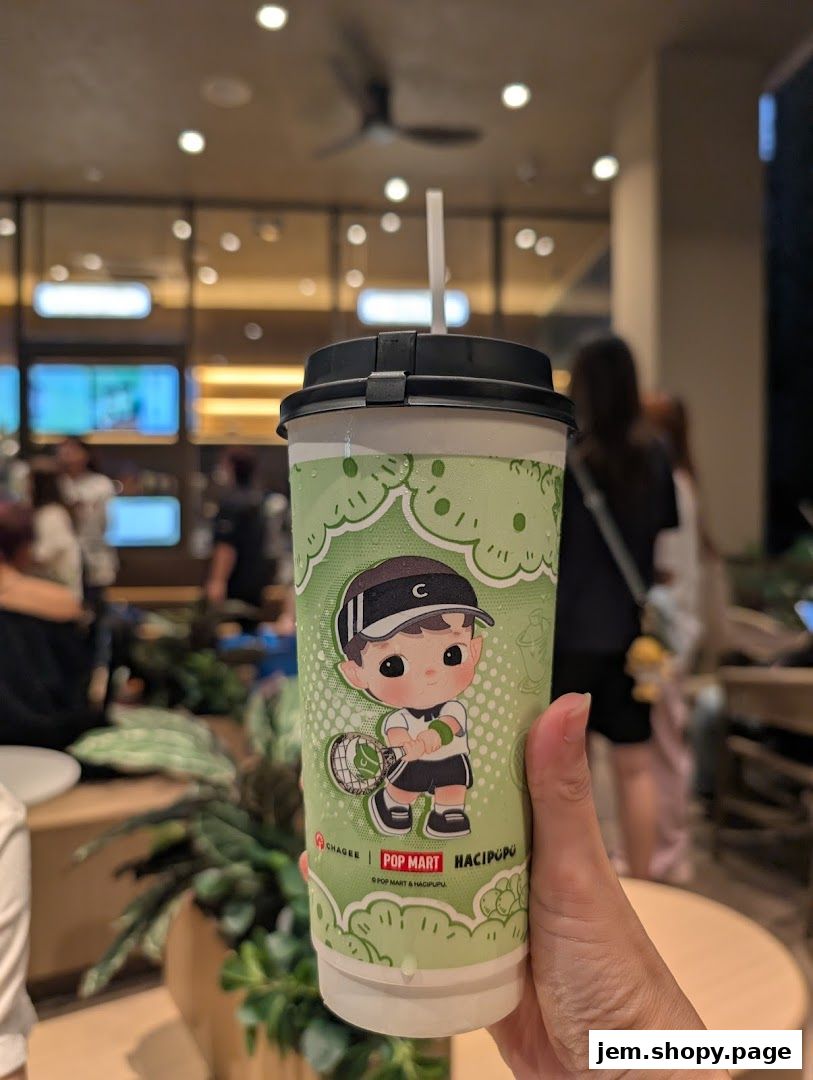 A hand holds a CHAGEE drink cup featuring a cute cartoon character.