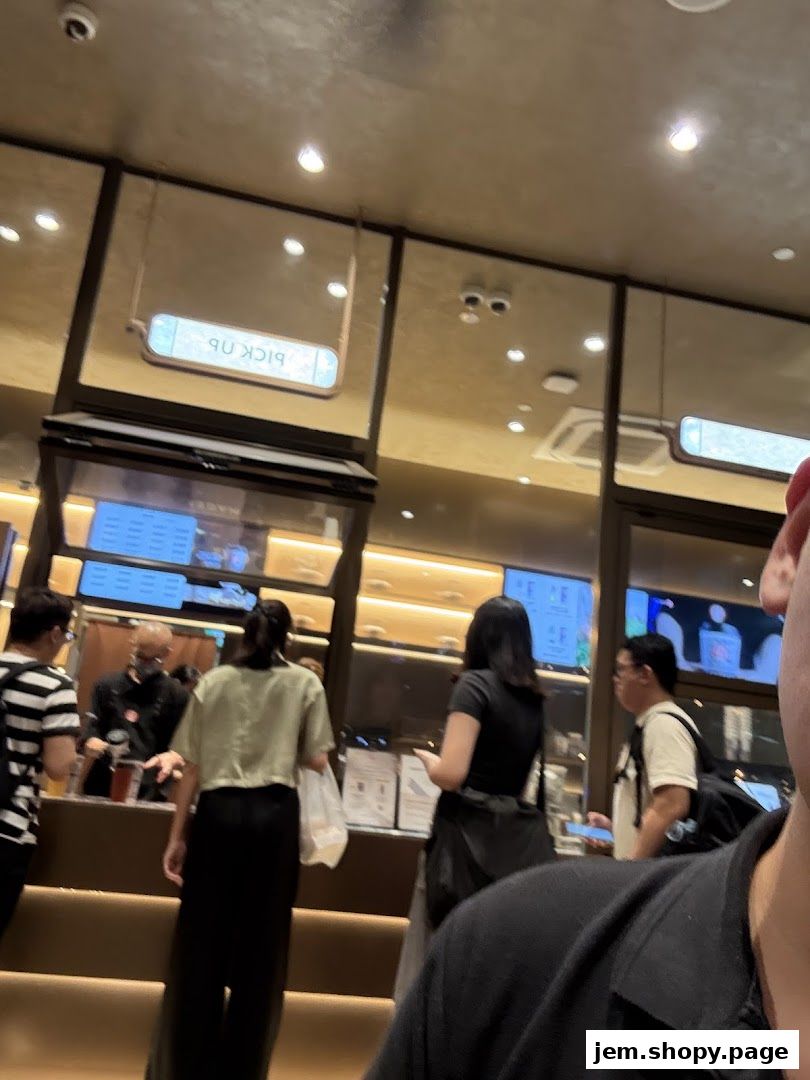 Customers queue at the counter of a modern beverage shop with digital menus.