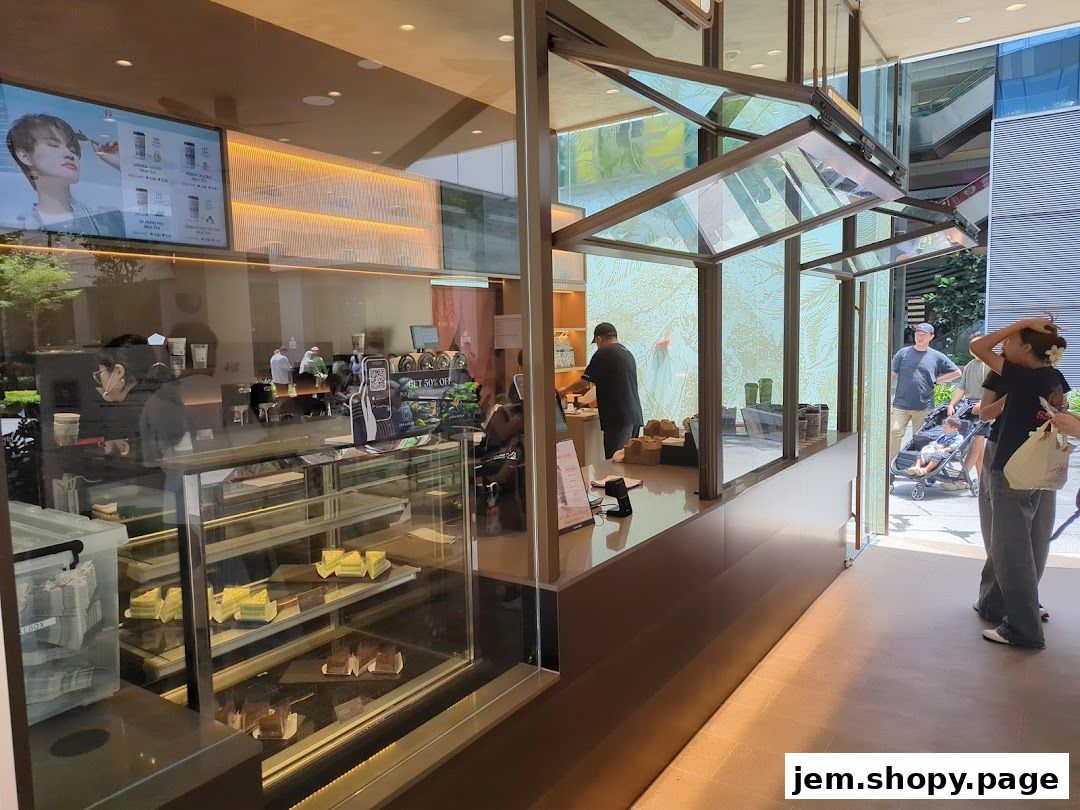 Interior view of a modern cafe with display cases of pastries and a digital menu board.