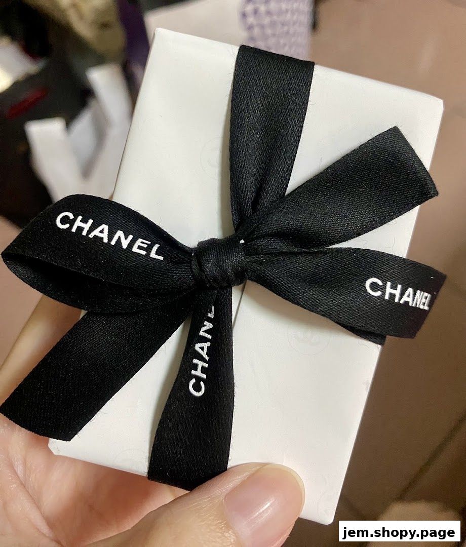 A hand holds a white gift box with a black Chanel ribbon tied in a bow.