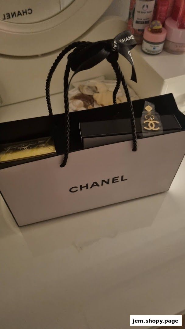 A Chanel shopping bag with a gift and earrings inside, on a reflective surface.