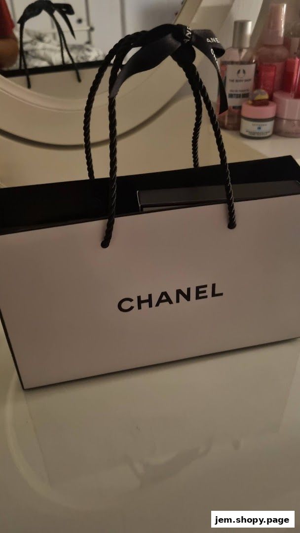 A Chanel shopping bag with black handles sits on a white surface.