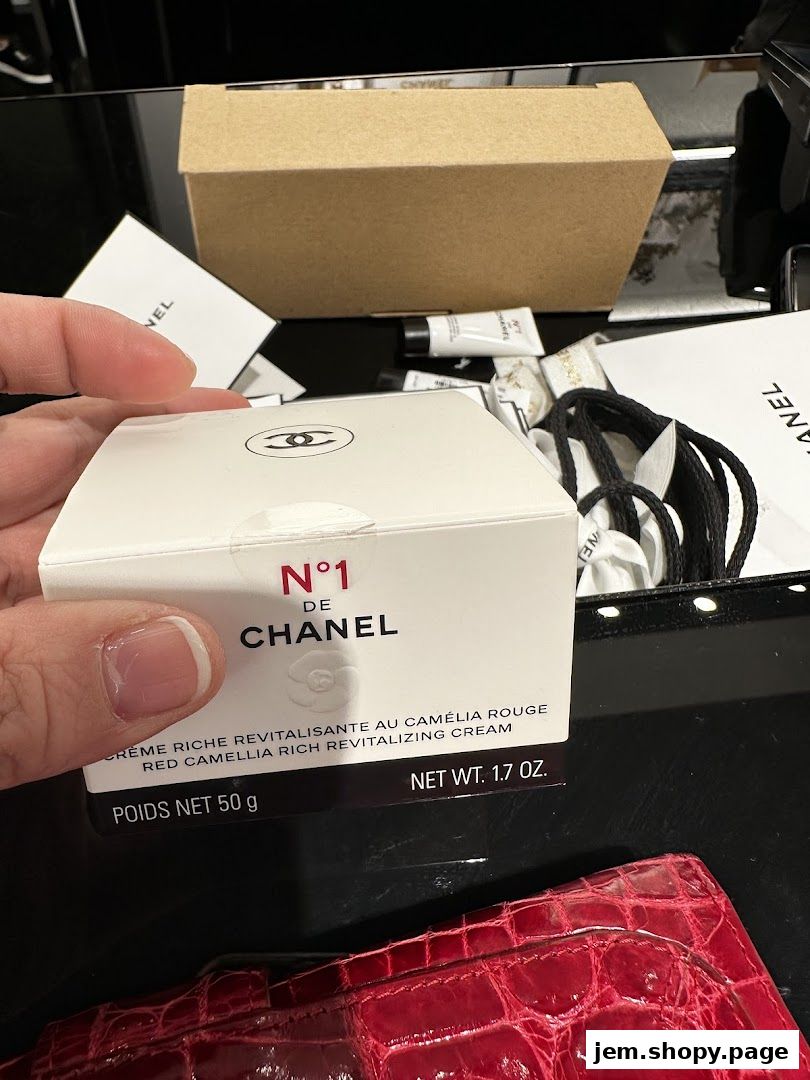 A hand holds a Chanel N°1 de Chanel Red Camellia Rich Revitalizing Cream box.