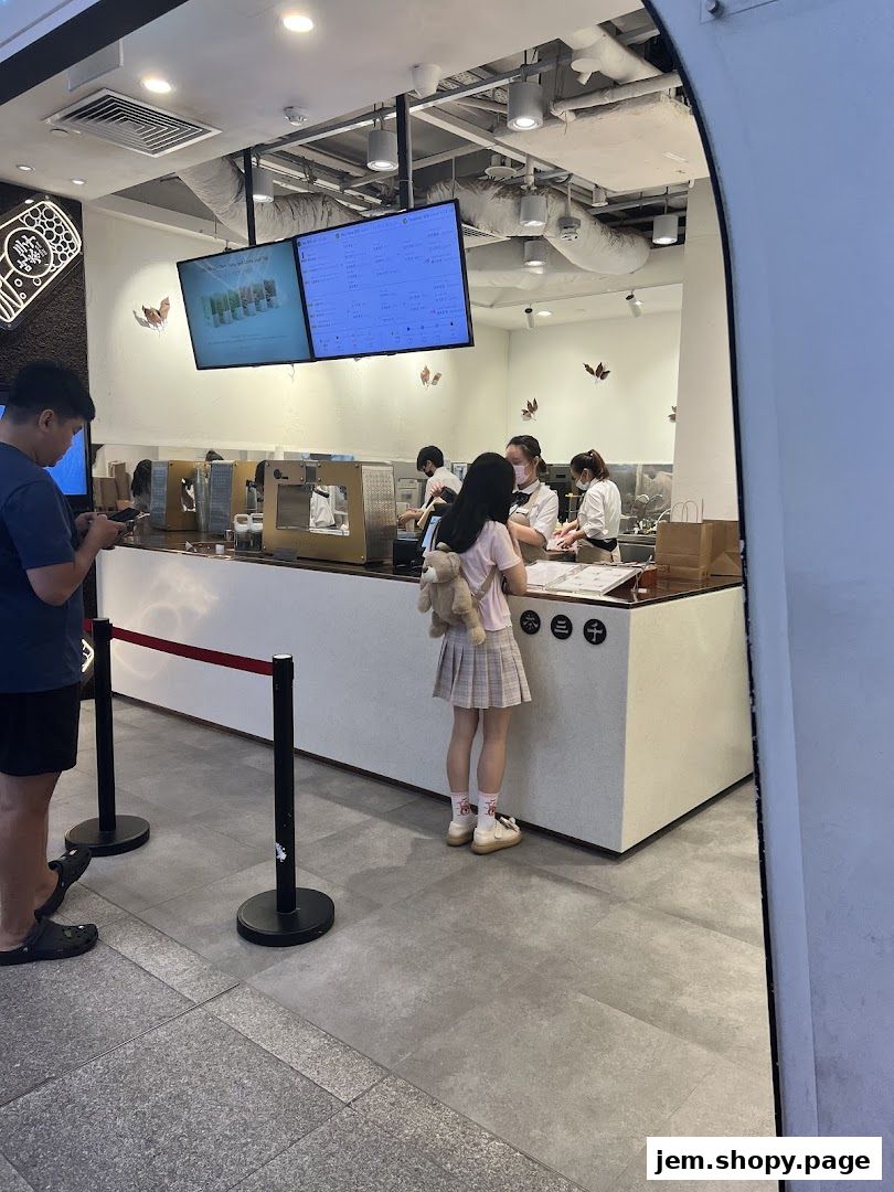 Customers ordering at a CHICHA San Chen bubble tea shop counter with digital menus.