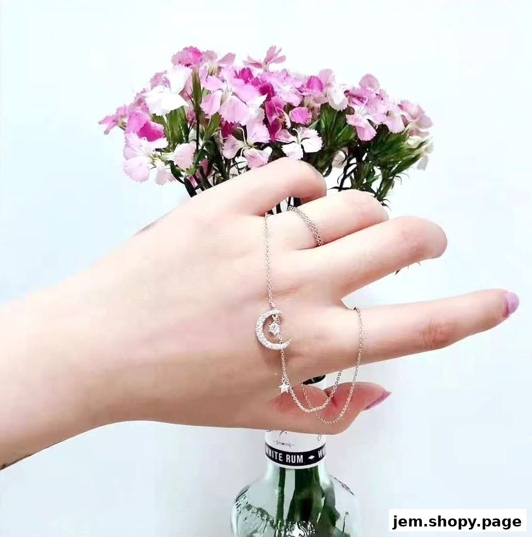 A hand wearing a delicate moon and star necklace with a bouquet of pink flowers.