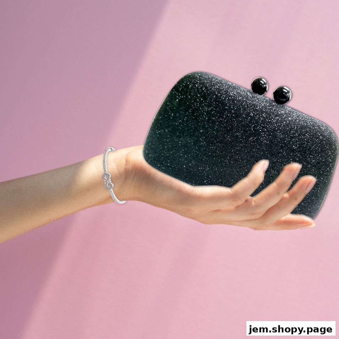 A hand wearing a bracelet holds a sparkling black clutch bag.