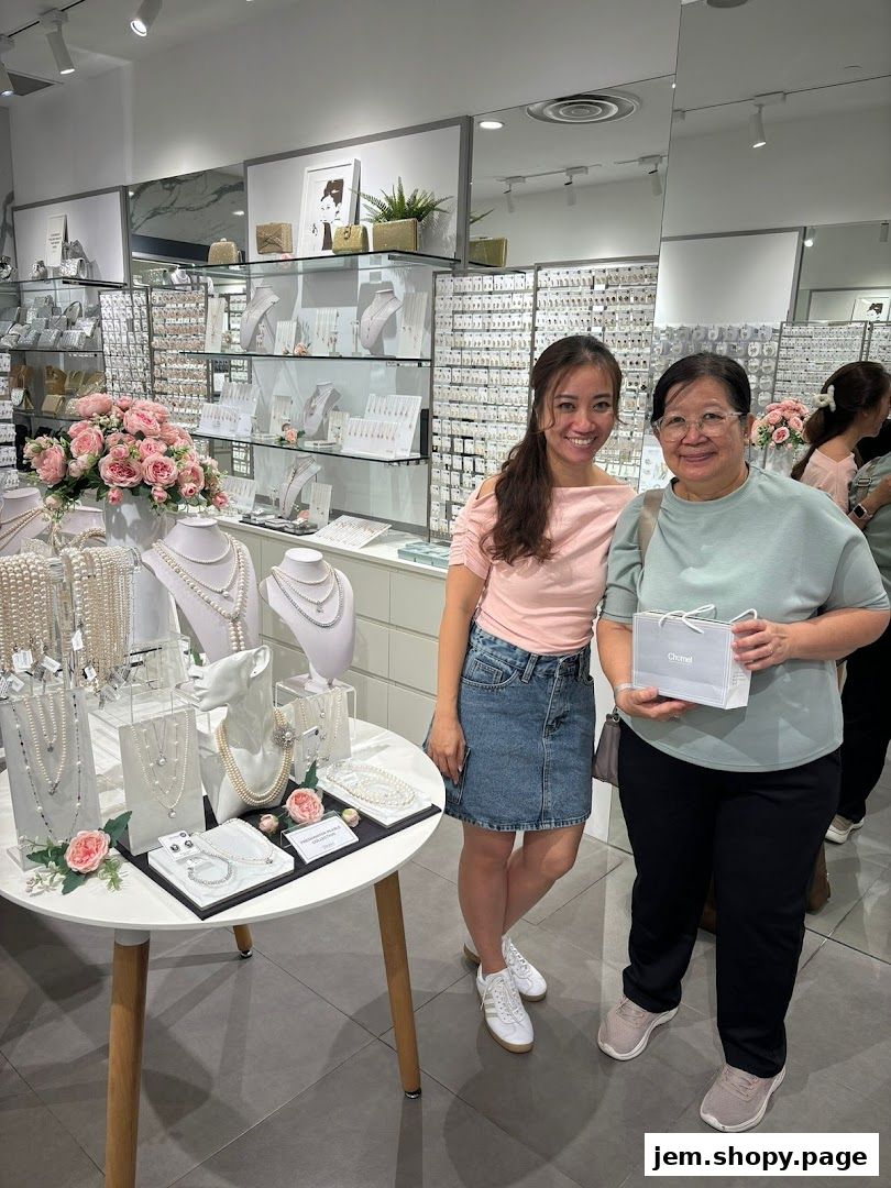 Two women smiling inside a jewelry store displaying pearl necklaces and earrings.