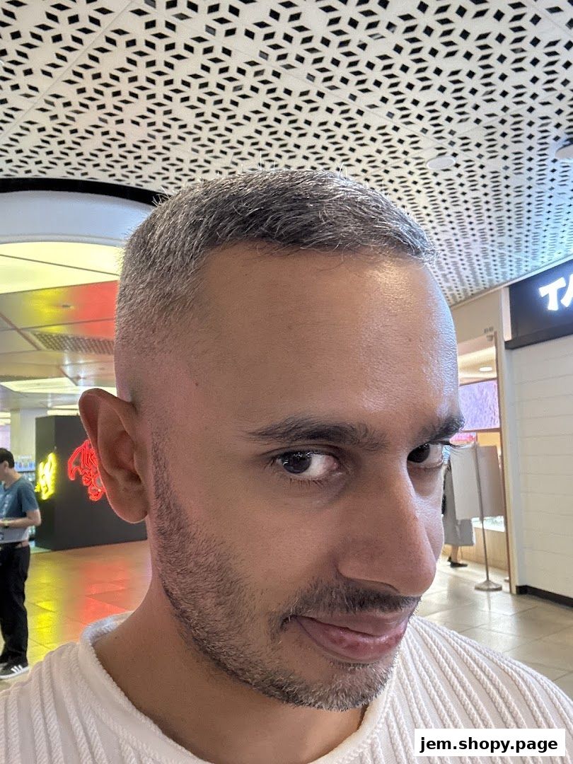 A man with a fresh haircut poses for a selfie inside a modern shopping mall.