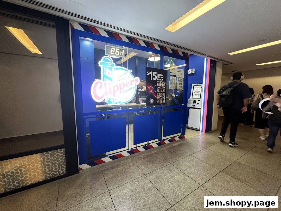 The exterior of Clippers Barber JEM, a barbershop with a blue and red striped awning and a prominent logo.