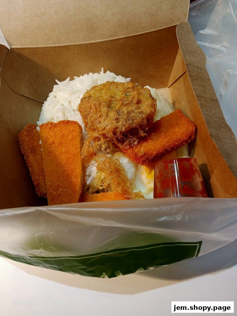 A close-up of a takeaway box filled with nasi lemak, fried items, and a fried egg.