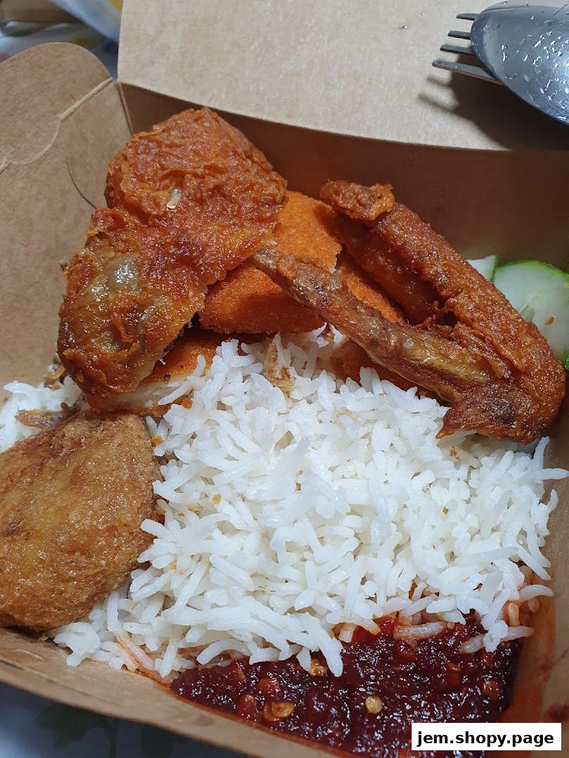 A close-up of a Nasi Lemak meal in a takeaway box with fried chicken and sambal.