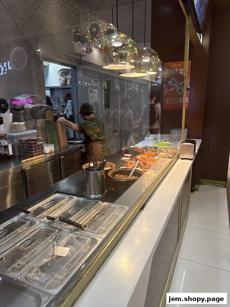 A food stall counter with various ingredients displayed and a staff member preparing food.