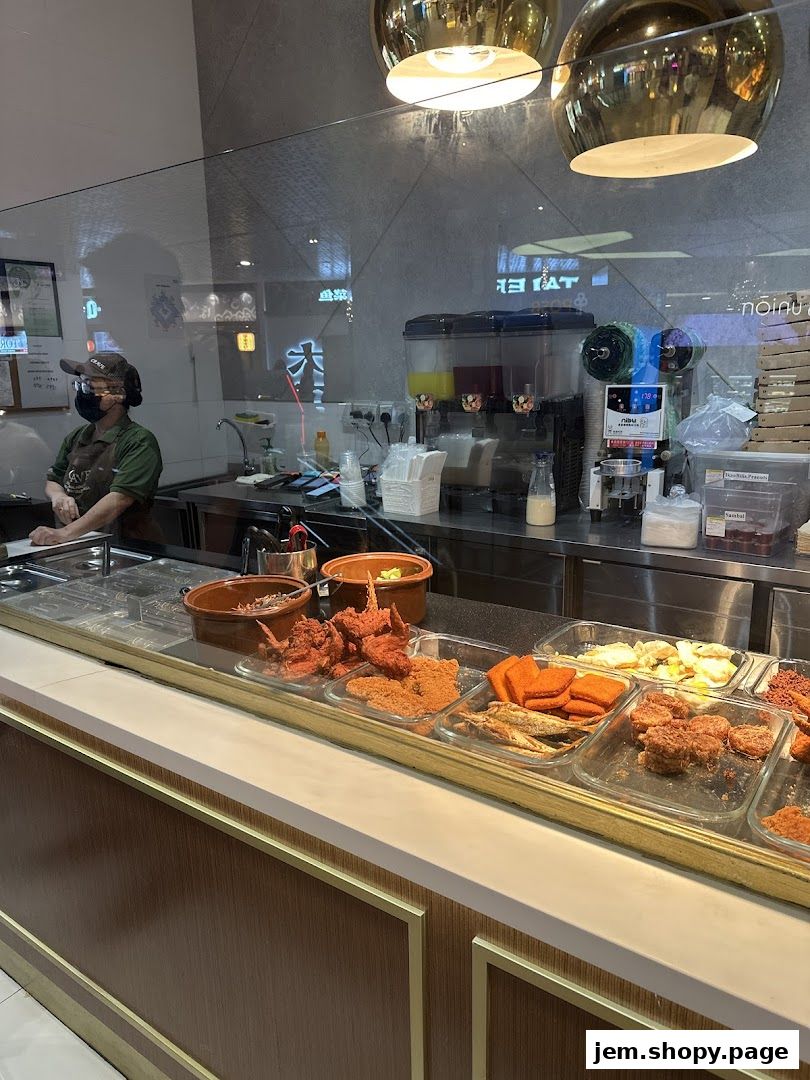 A food counter displaying various fried items and drinks, with a staff member behind the counter.