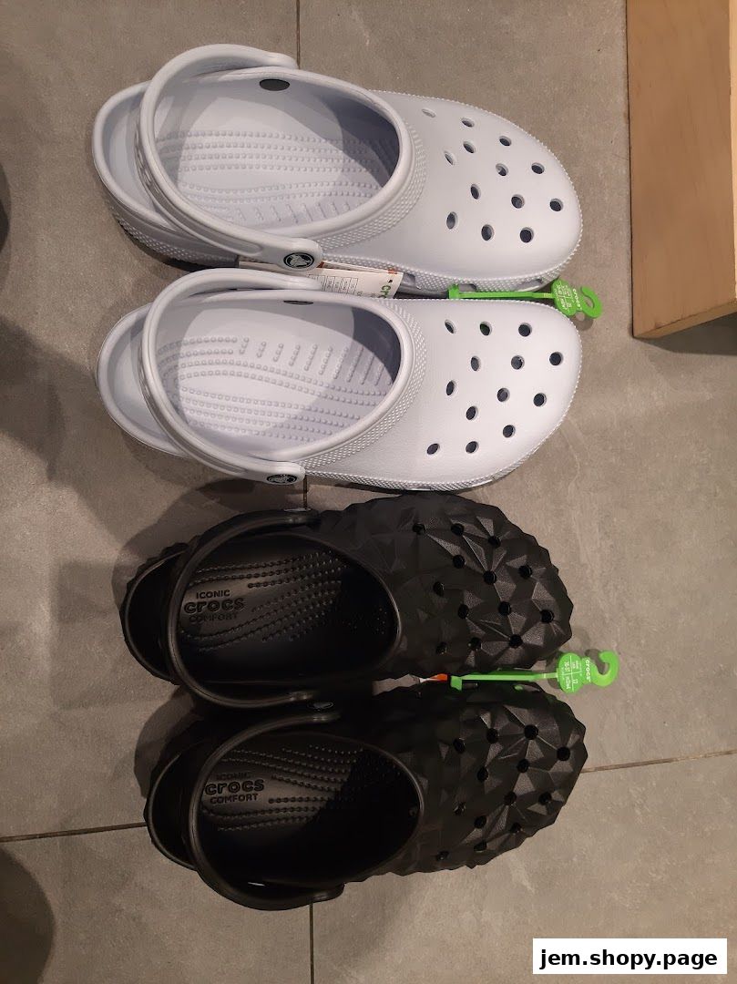 Two pairs of Crocs shoes, one white and one black, displayed on a tiled floor.