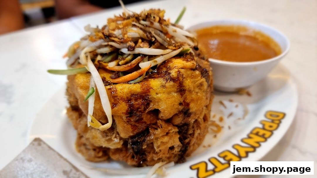 A close-up of a fried dish topped with vegetables and a side of sauce, served on a plate with the shop's logo.