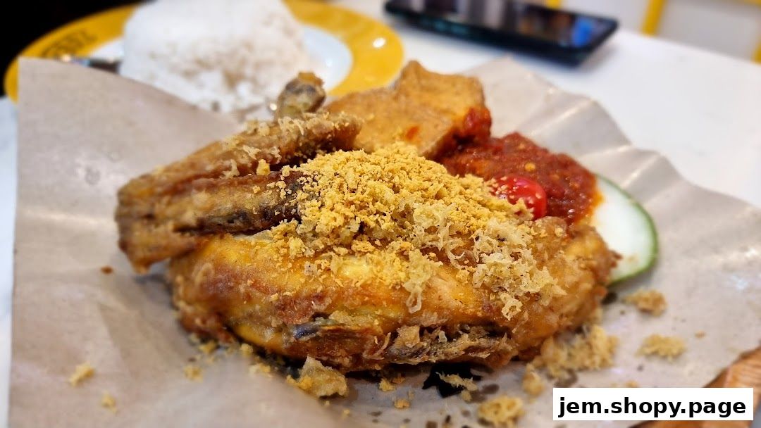 A close-up of a crispy fried chicken dish with rice, tofu, chili sauce, and cucumber.