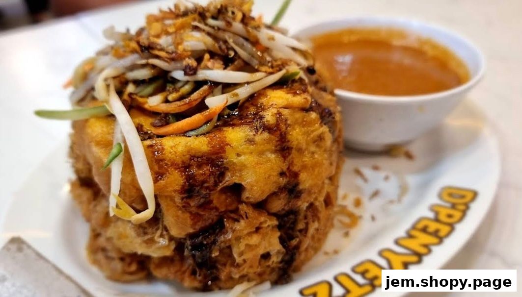 A close-up of a deep-fried dish topped with vegetables and sauce, served with a side of dipping sauce.