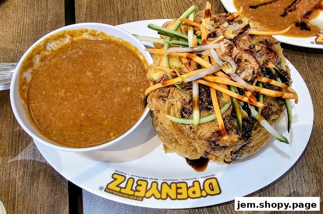 A close-up of a crispy fried dish topped with vegetables and a side of peanut sauce.