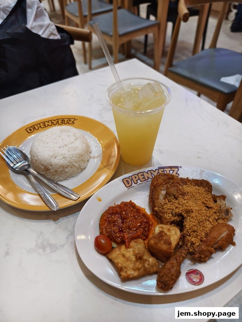 A plate of fried chicken with rice, chili sauce, and a refreshing drink.