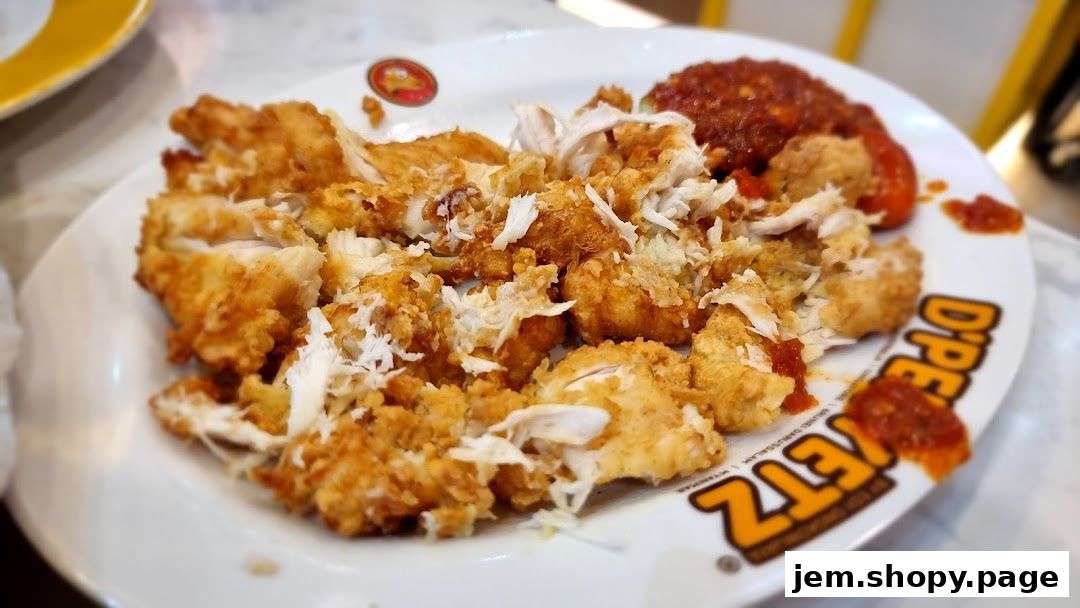 A plate of crispy fried chicken pieces with a side of spicy red sauce.