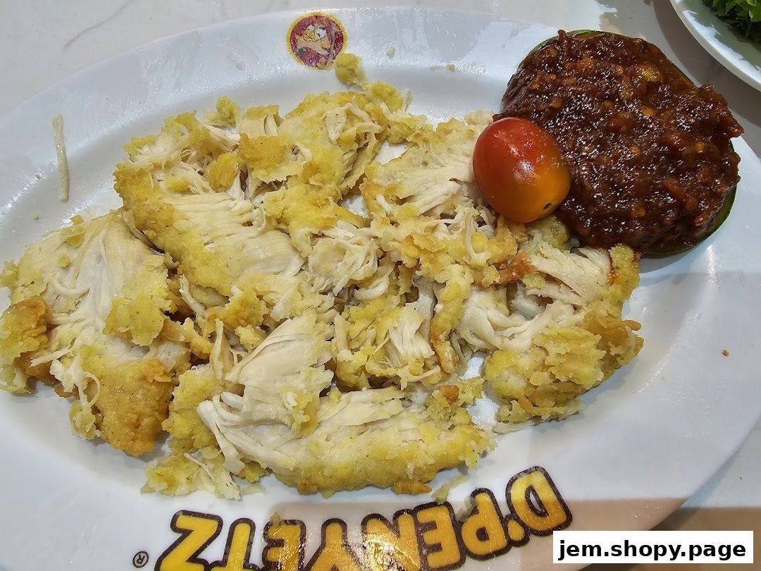 A plate of shredded fried chicken with sambal and a cherry tomato.