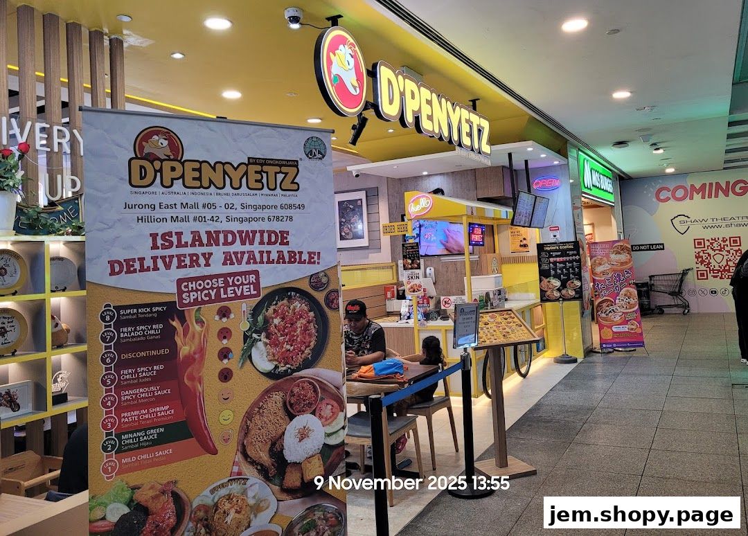 The exterior of a D'Penyetz restaurant with a banner advertising islandwide delivery and spicy levels.