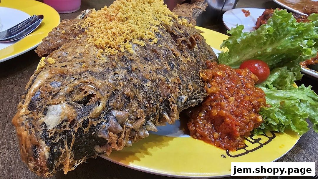 A crispy fried fish dish served with sambal, lettuce, and tomato on a yellow plate.