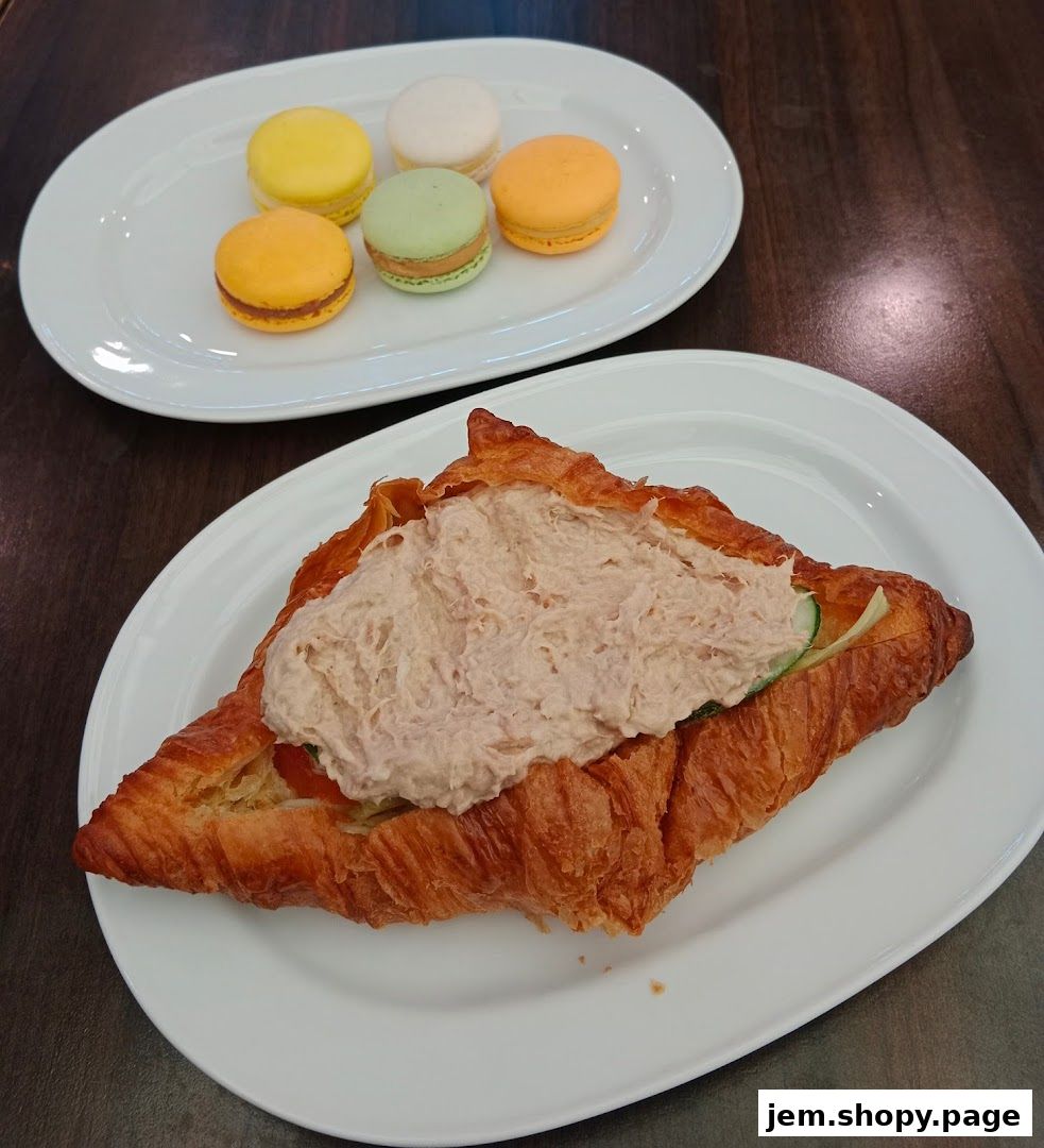 A croissant sandwich filled with tuna salad and a plate of colorful macarons.