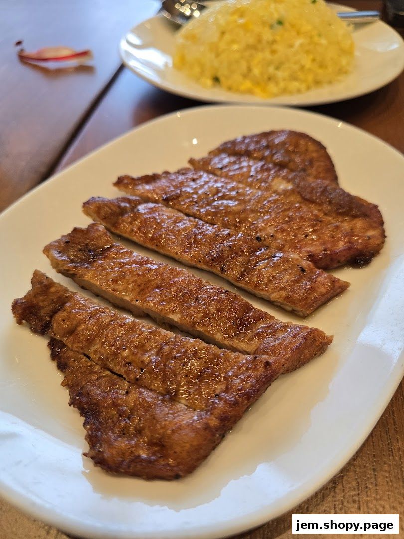 A plate of sliced, pan-fried pork belly with a side of fried rice.