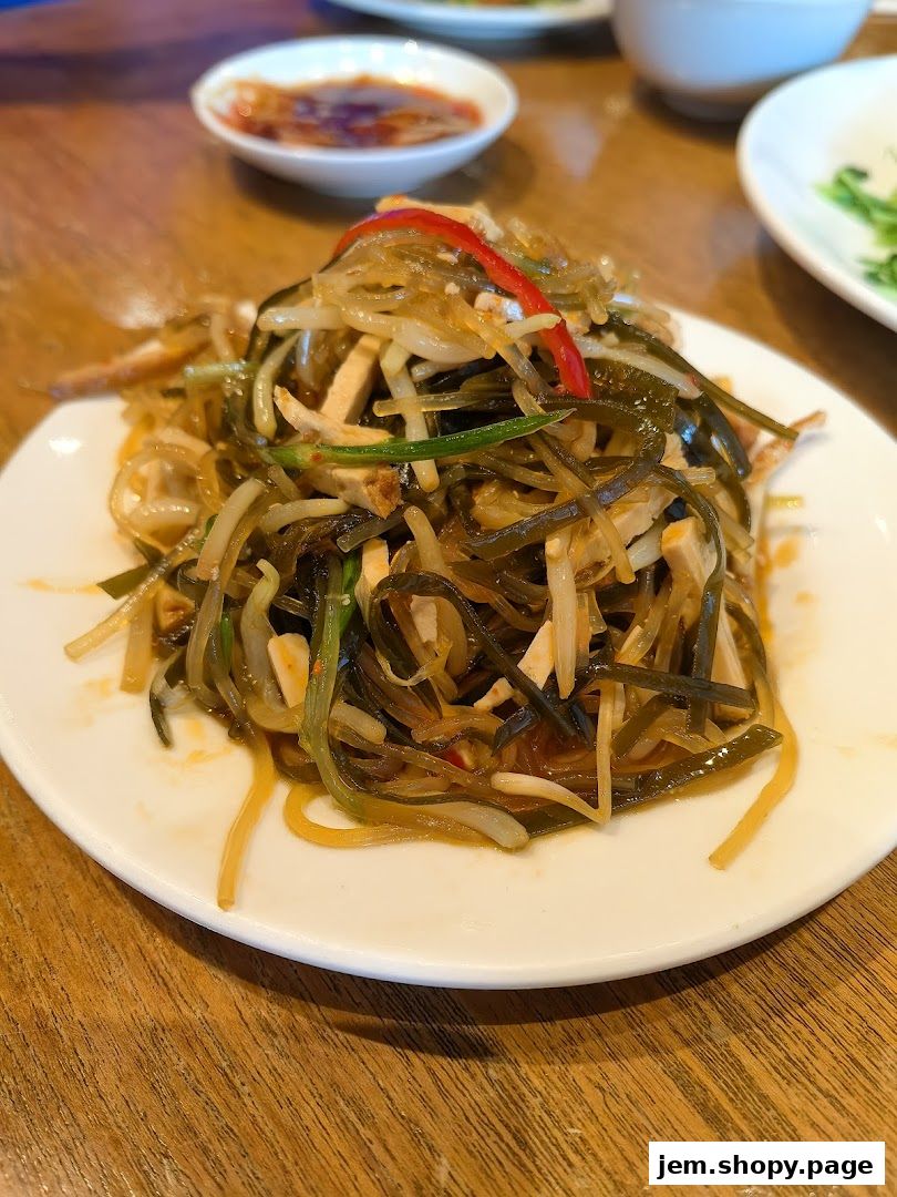 A plate of seaweed salad with tofu and red pepper strips on a wooden table.