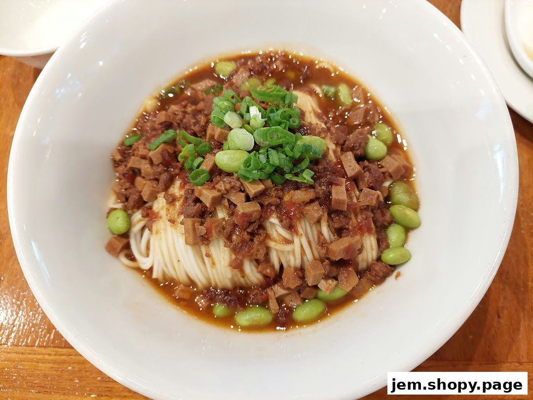 A bowl of noodles topped with minced meat, edamame, and scallions in a savory sauce.