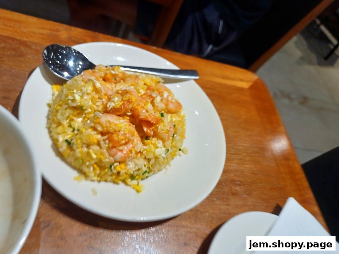 A plate of shrimp fried rice with a spoon on a wooden table.