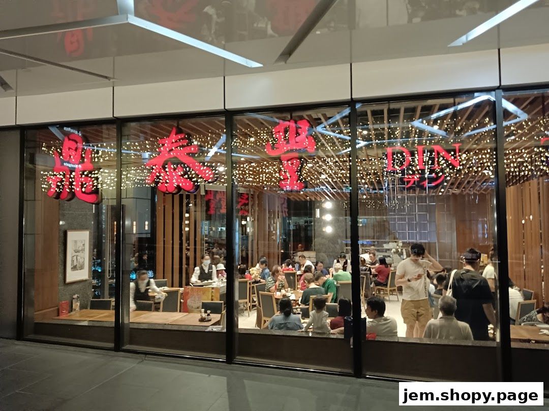 View of Din Tai Fung restaurant interior through large glass windows, showing diners and decor.