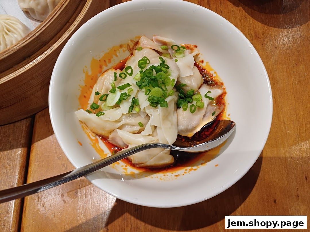 A bowl of delicious wontons in chili oil, garnished with chopped scallions.
