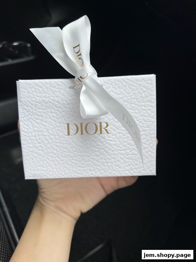 A hand holds a white Dior gift box tied with a branded ribbon.