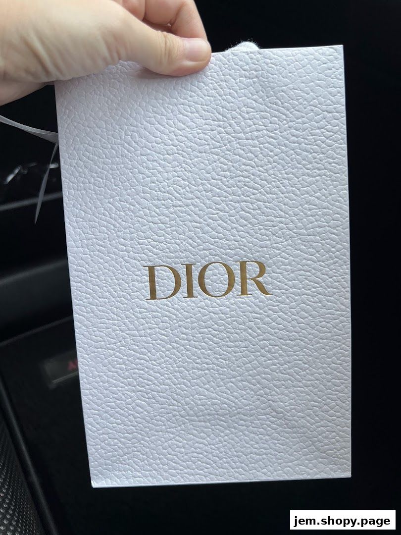 A hand holds a white textured Dior branded gift bag with gold lettering.