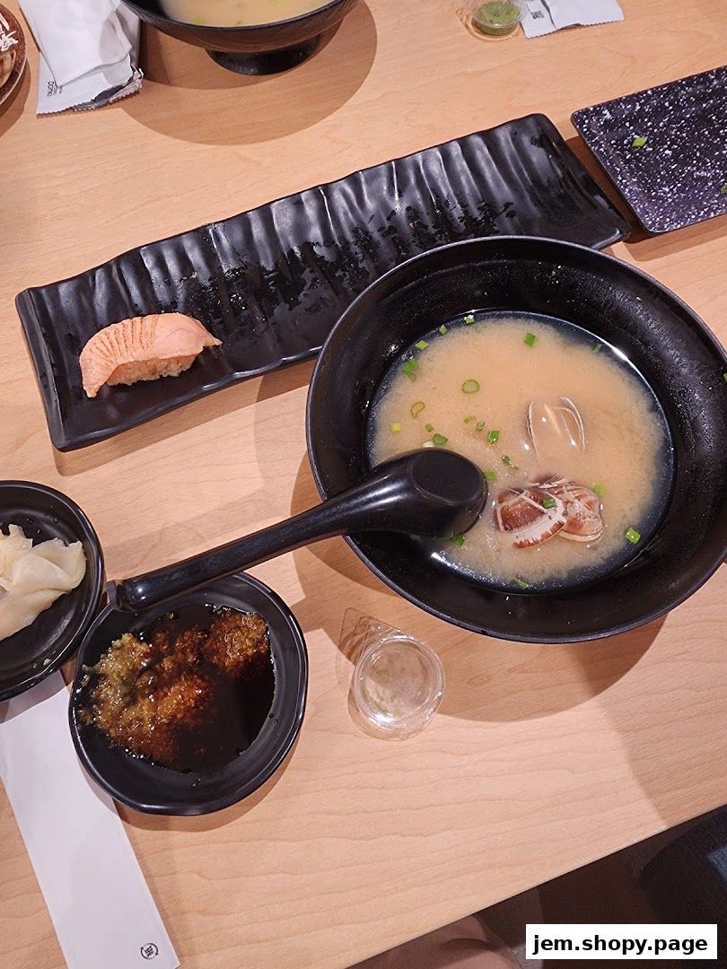 A table setting with miso soup, sushi, and dipping sauce.