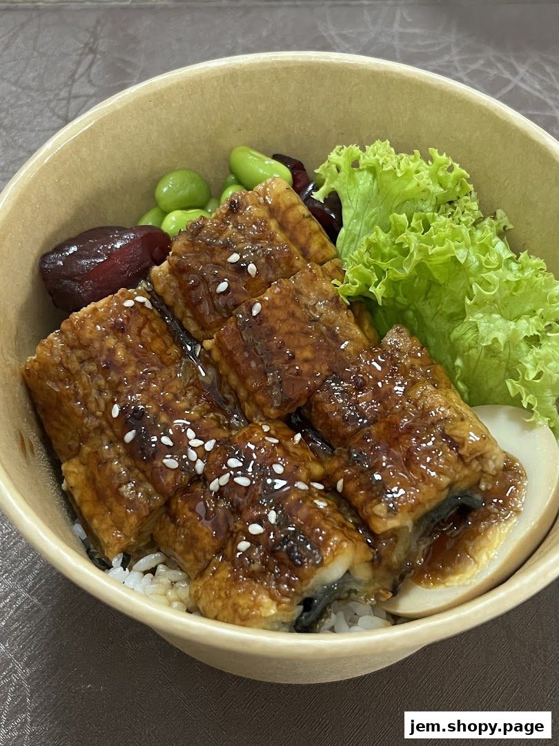A bowl of rice topped with grilled eel, edamame, and lettuce.