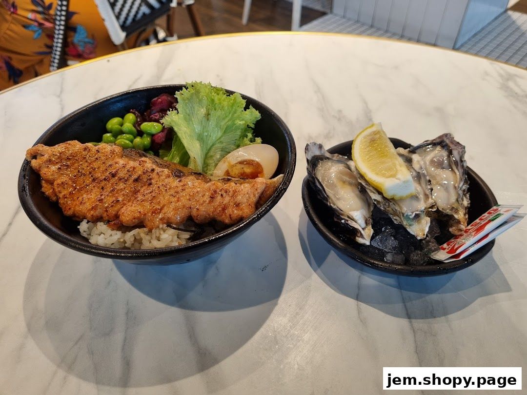 A bowl of grilled salmon with rice and a side of fresh oysters with lemon.