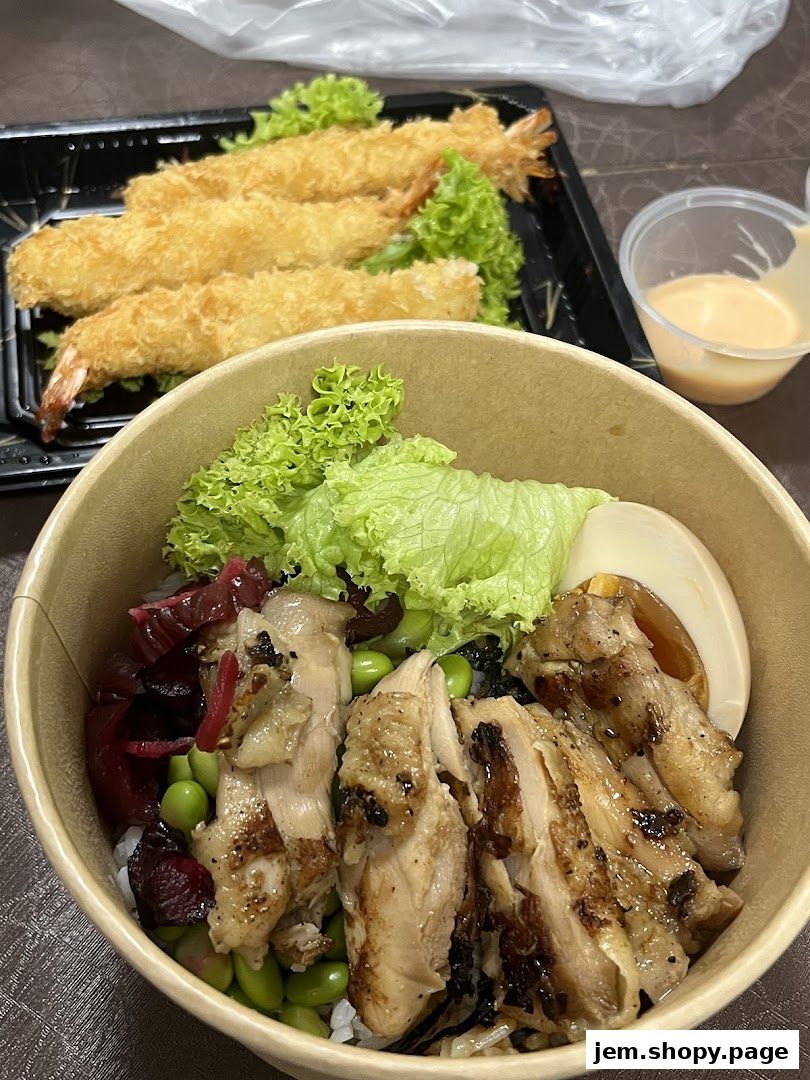 A bowl of rice with grilled chicken, edamame, and pickled vegetables, served with fried shrimp.