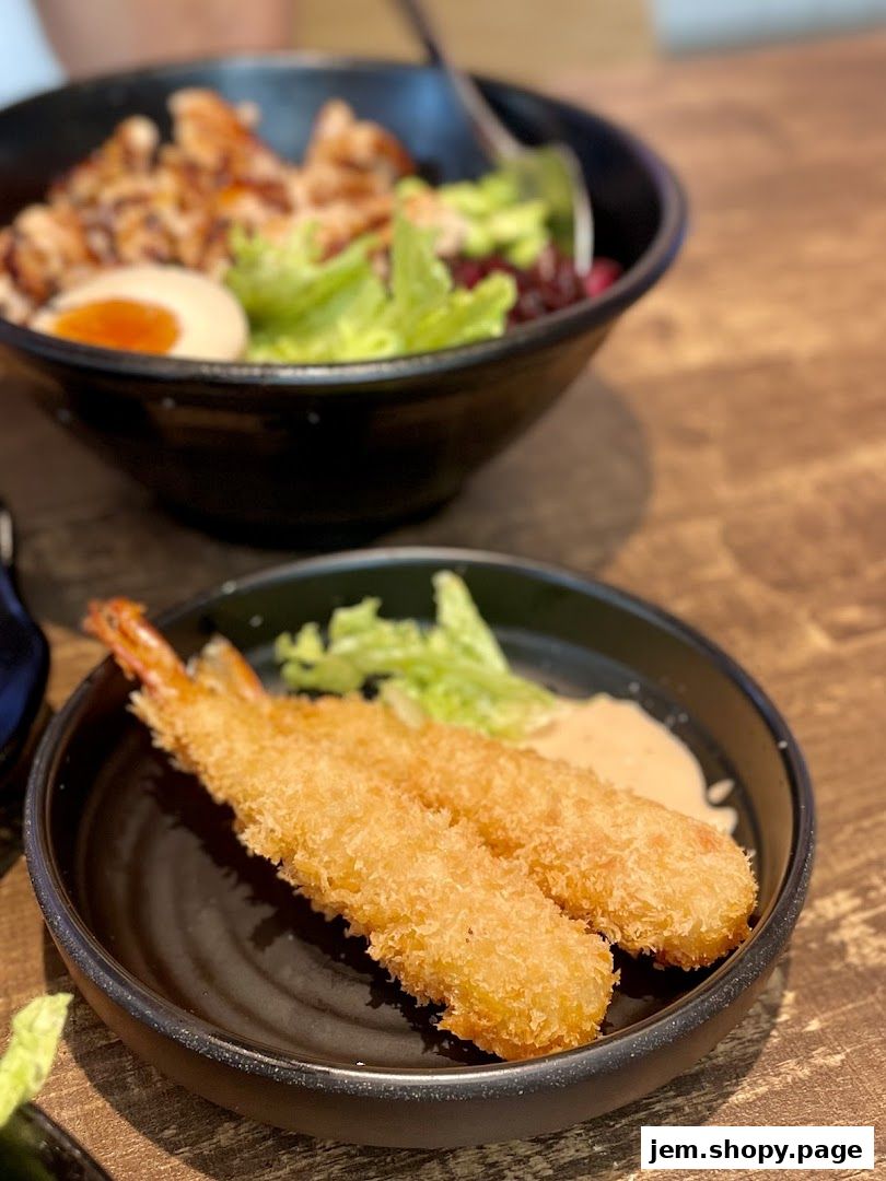Crispy fried shrimp served with a side of sauce and a bowl of rice with egg and salad.