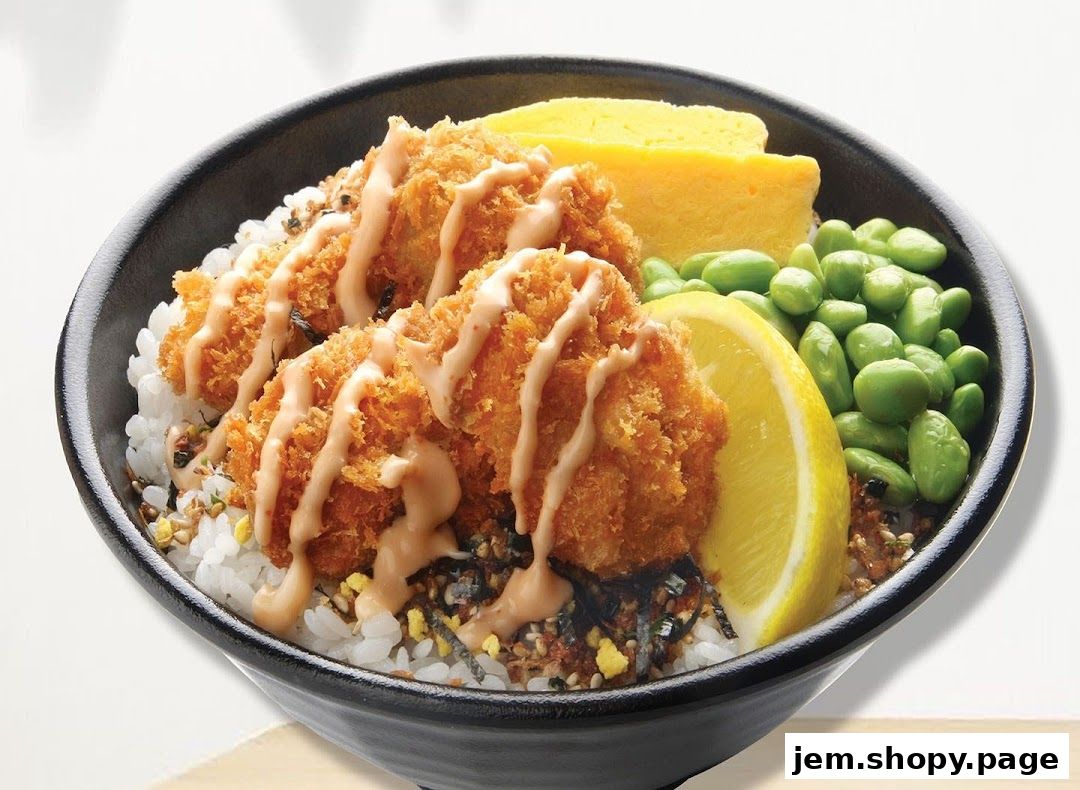 A close-up of a delicious oyster donburi bowl with fried oysters, rice, edamame, and a lemon slice.