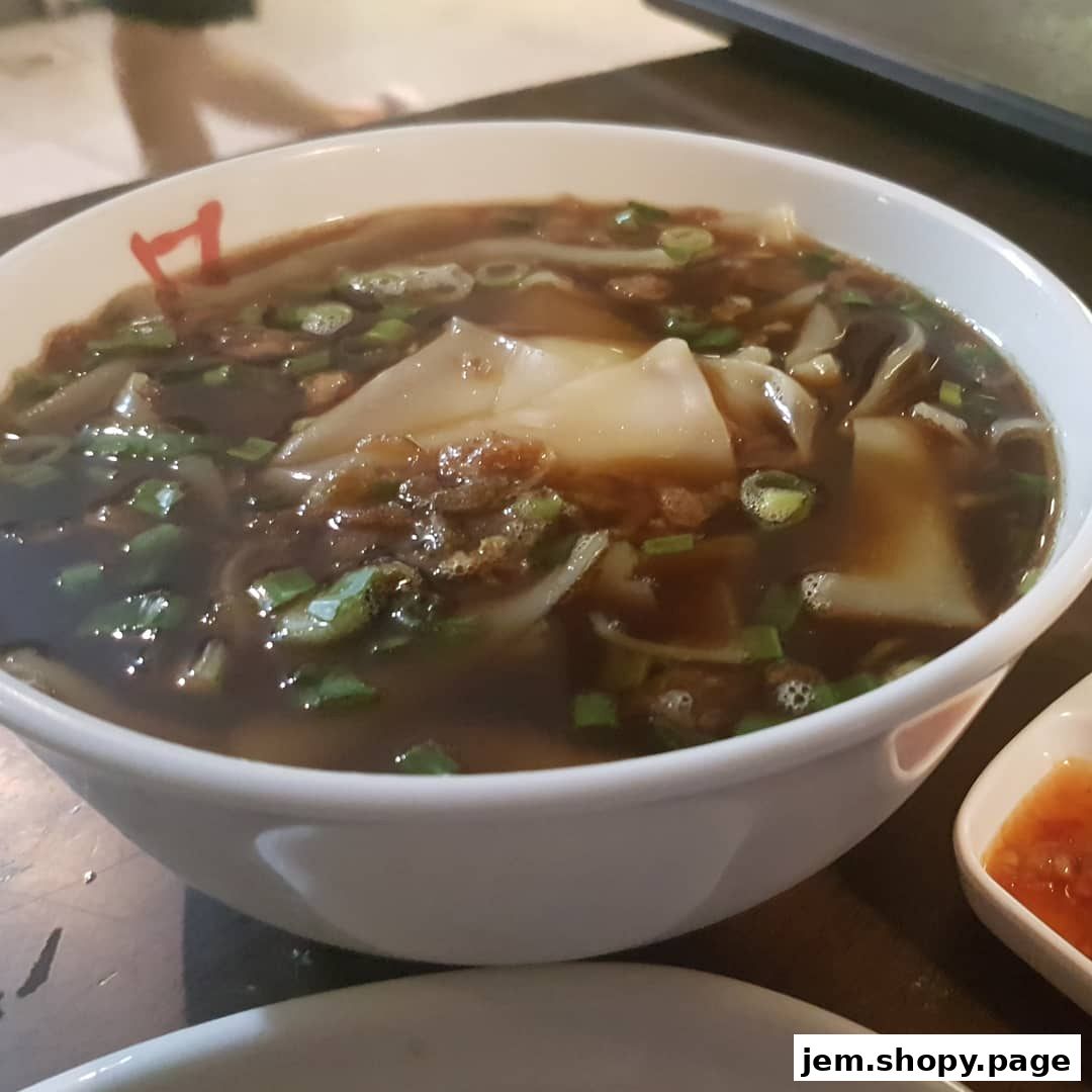 A close-up of a steaming bowl of Teochew Kway Chap with noodles and meat.