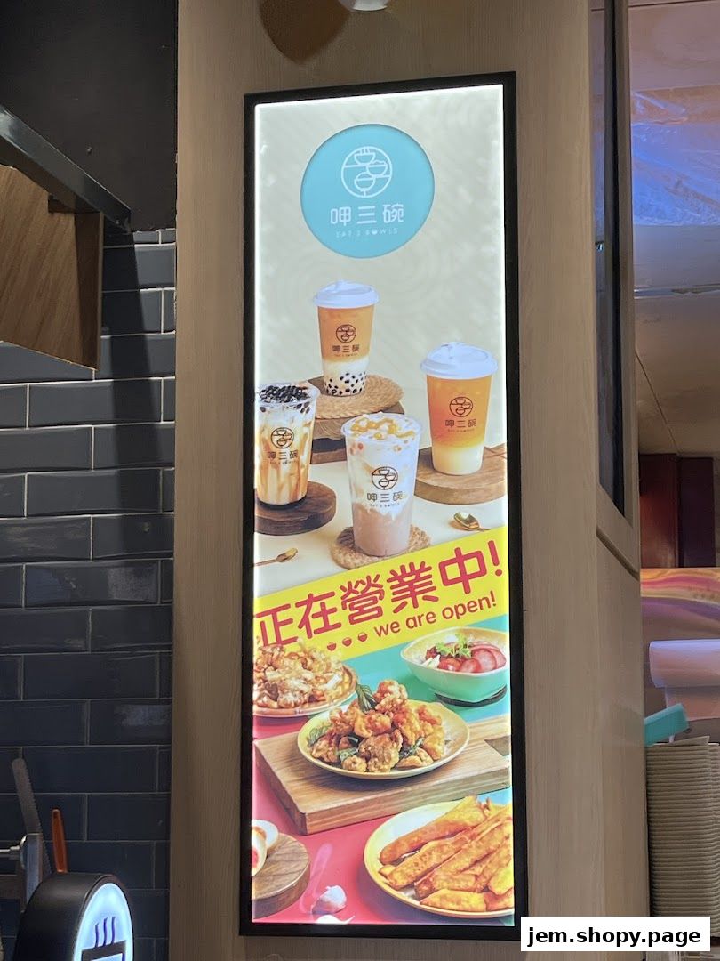 A vertical illuminated sign showcasing bubble tea and food items from Eat 3 Bowls.