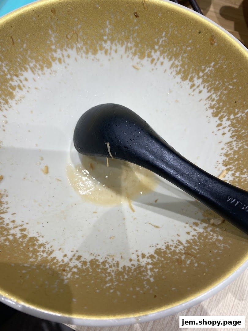 A close-up of a nearly empty bowl with a black spoon resting inside.