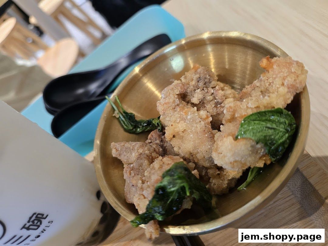 A close-up of crispy fried chicken with basil leaves in a brass bowl, next to a drink.