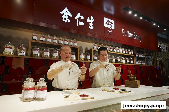 Two men in white coats weigh traditional Chinese medicine ingredients behind a counter.